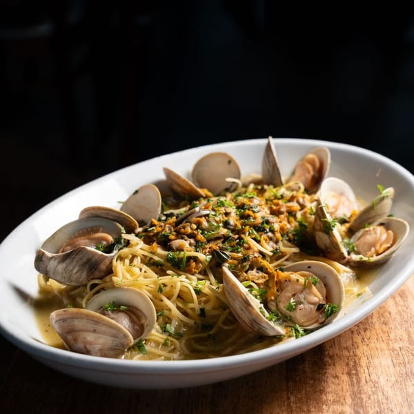 Spaghetti with clams, garlic, and parsley in a white oval bowl on a wooden surface.