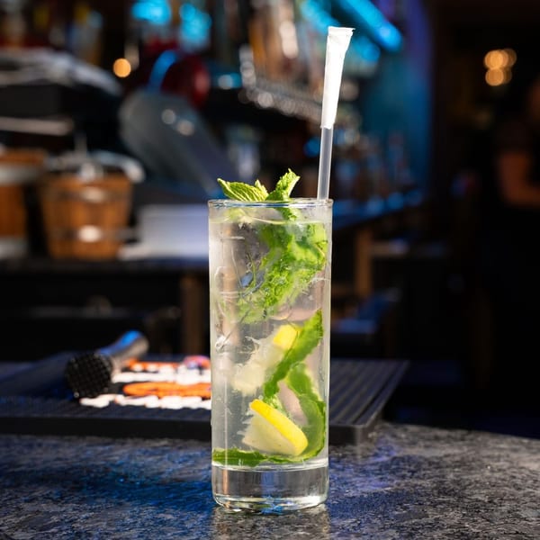 Tall glass of mojito with mint, lemon, and a straw on a dark bar counter.