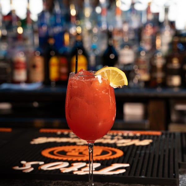 Red cocktail in a wine glass with lemon and straw on a bar counter.