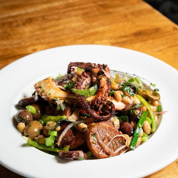 Grilled octopus with roasted potatoes, white beans, olives, and green onions on a wooden table.