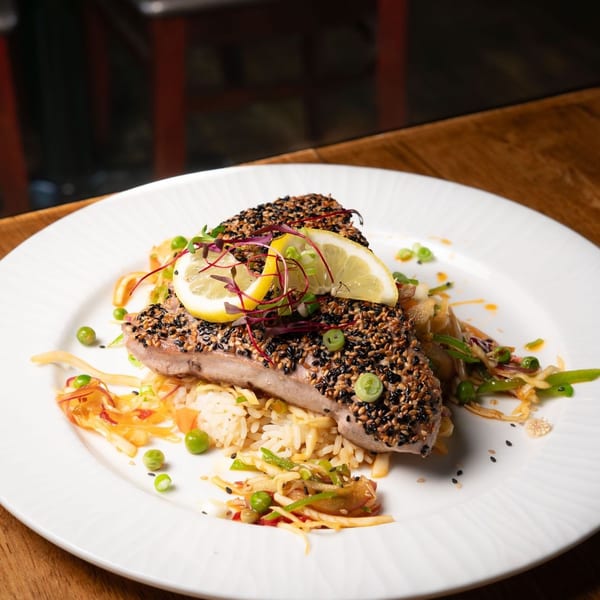 Sesame-crusted tuna steak served over rice and vegetables, garnished with lemon and microgreens.